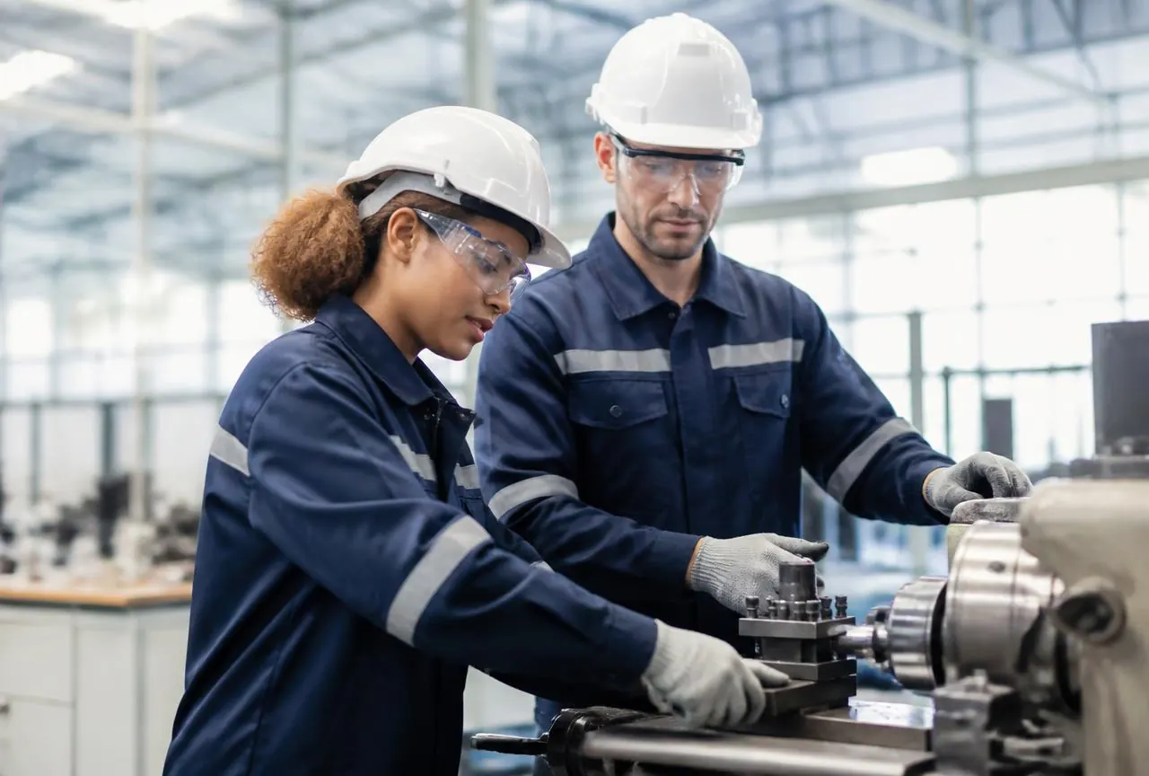 Two manufacturing employees in hard hats and safety glasses operating machinery
